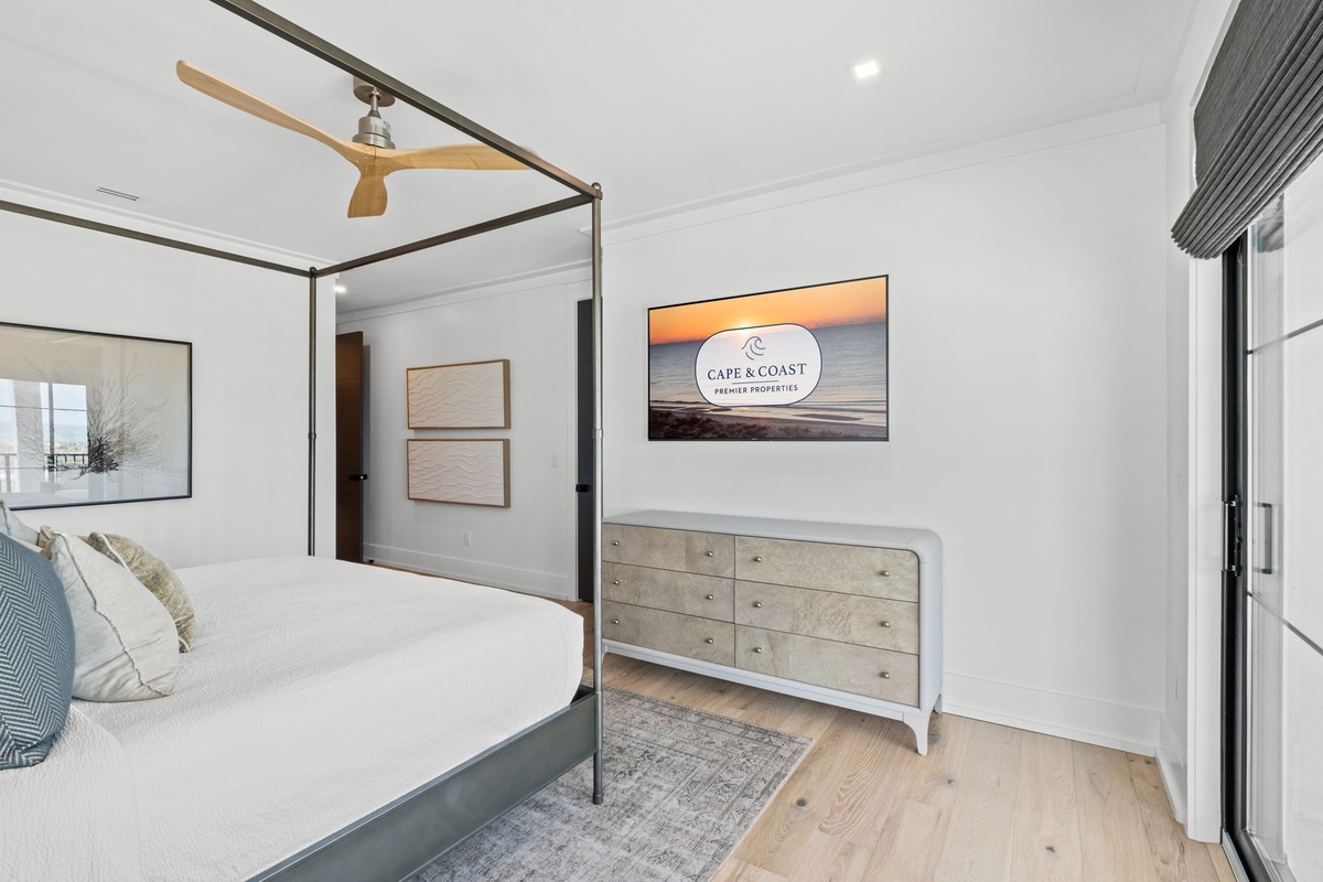 Slip into crisp linens beneath the modern canopy bed, your coastal retreat set to the gentle rhythm of the ceiling fan overhead. Soft blues, warm wood tones, and seaside art create your tranquil escape.