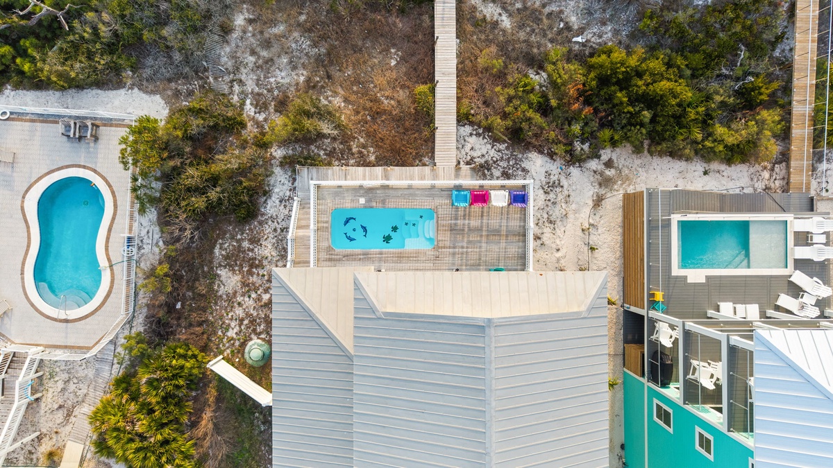 Aerial view of beachfront property featuring multiple swimming pools, modern architecture, and pristine natural surroundings.