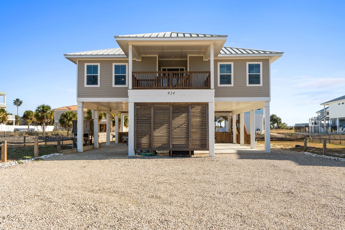 Modern coastal rental home featuring elevated design with covered parking and beach-style architecture near palm-lined surroundings.