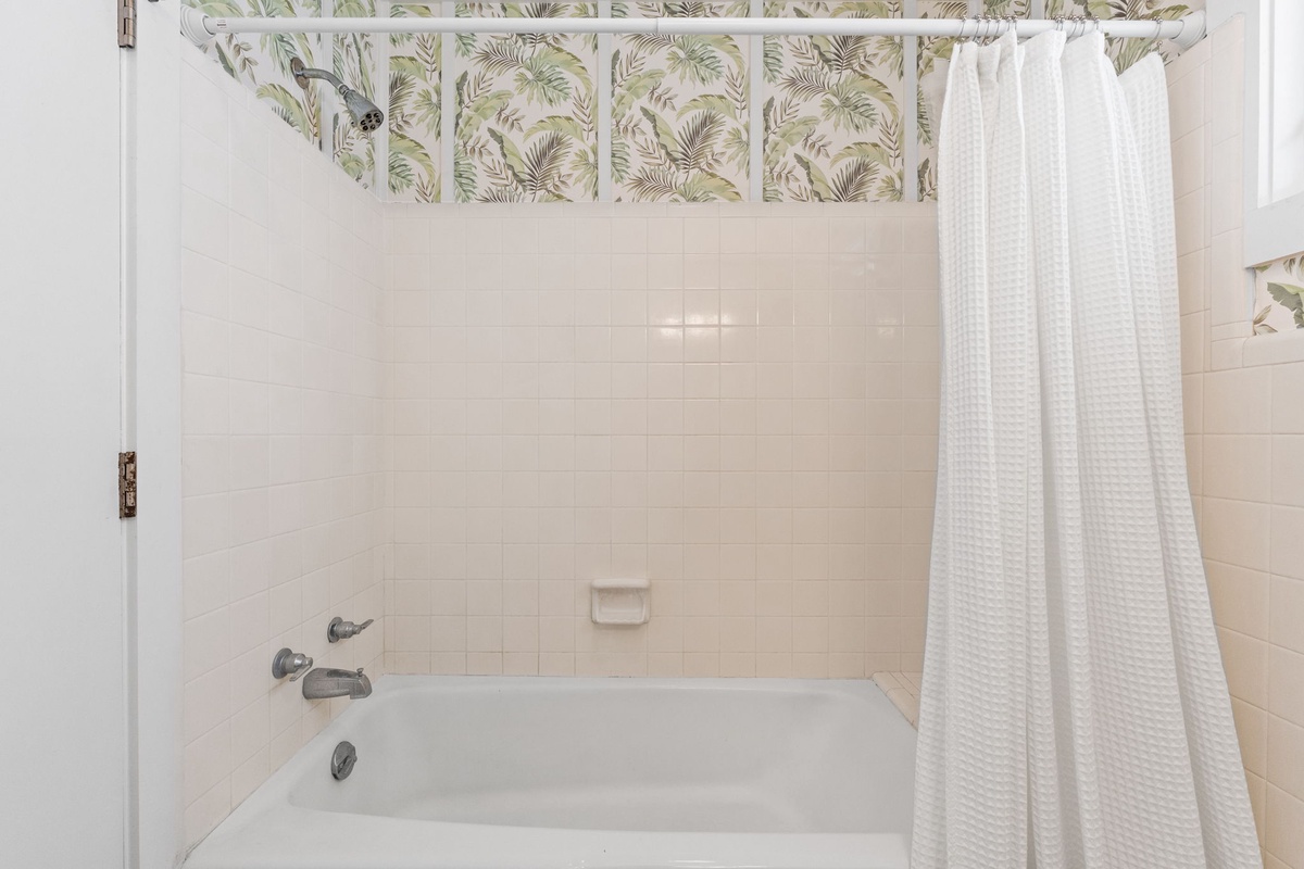 Step into your pristine bathroom, where a deep soaking tub awaits beneath cheerful botanical wallpaper. Crisp white tile and fresh towels create a calming retreat for your unwinding.
