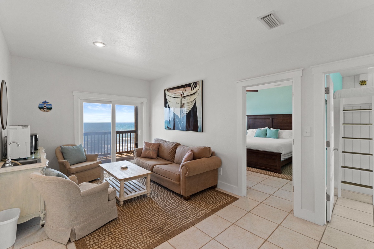 Picture yourself relaxing in this bright, coastal-inspired space. Soft earth tones and pops of aqua invite you to unwind while the open layout connects your living area to the bedroom. That balcony view promises morning coffee by the sea.