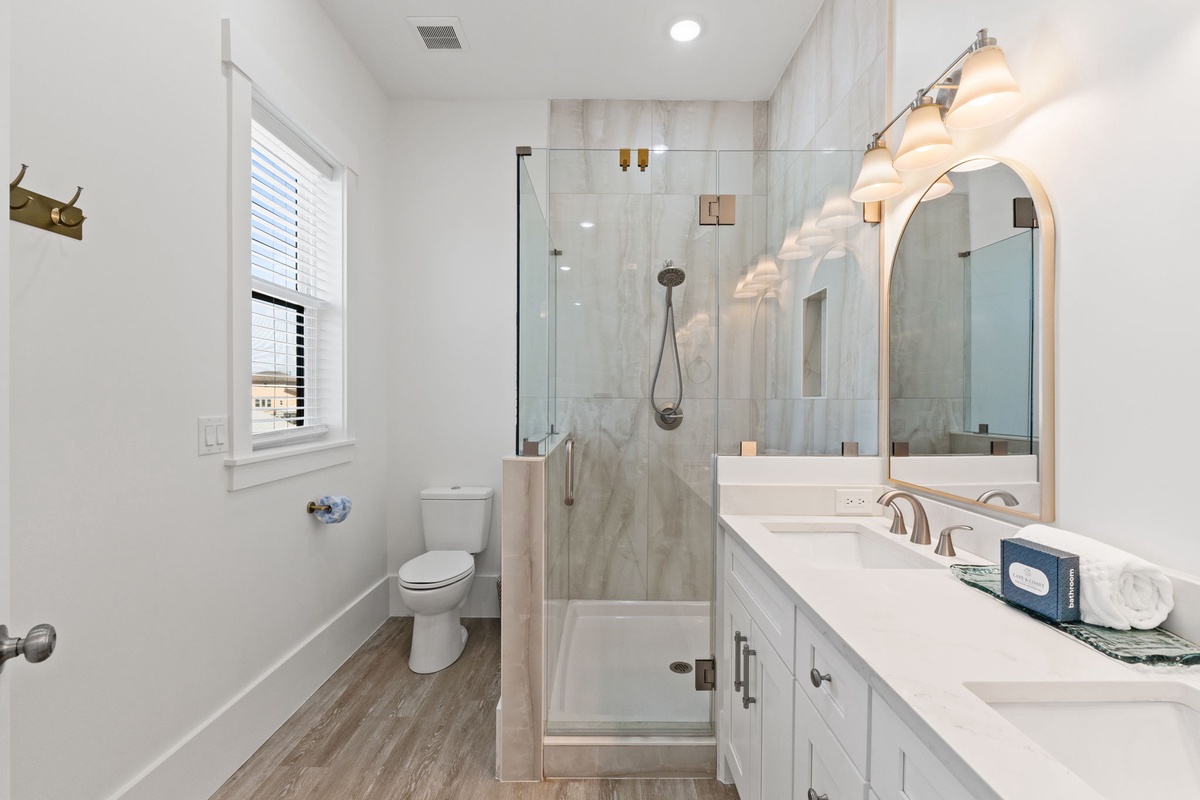 Indulge in your spa-like bathroom featuring marble shower walls, elegant vanity lighting, and crisp white finishes for ultimate relaxation.