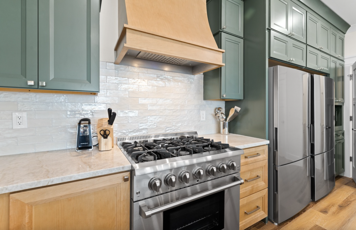 Your gourmet kitchen features professional-grade appliances, elegant green cabinetry, and marble countertops perfect for creating memorable meals together.