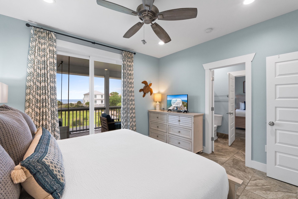 Relax in your serene coastal bedroom with plush linens, gentle ceiling fan breezes, and a private balcony framing peaceful green views and distant horizons.