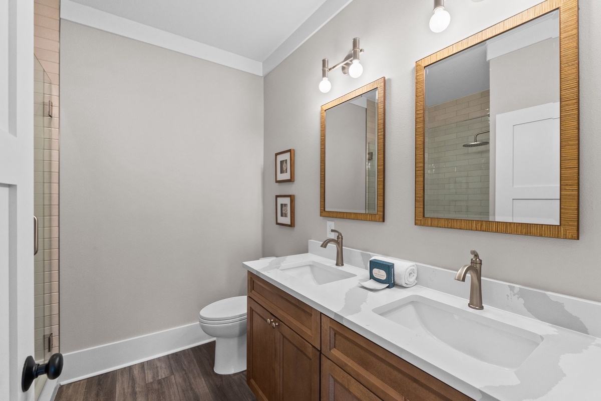 Refresh in your elegant dual-sink bathroom, featuring warm wood tones, bright lighting, and a sleek shower—perfectly styled for your comfort and convenience.