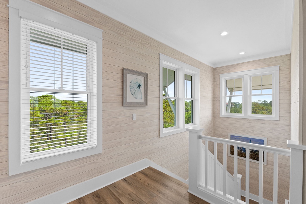 Bright natural light fills this airy upstairs landing, where soft wood tones and large windows frame peaceful views of lush greenery—your tranquil spot to pause and unwind between spaces.