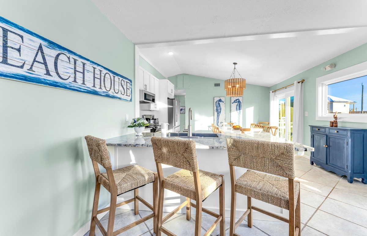 Step into your coastal kitchen where sea-green walls and wicker bar stools create the perfect beachy vibe for morning coffee.