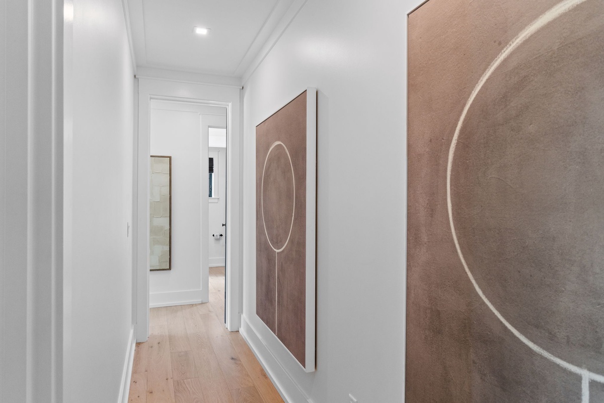 A bright hallway with contemporary art leads you through the home, where soft lighting and warm wood floors create a welcoming flow between rooms.