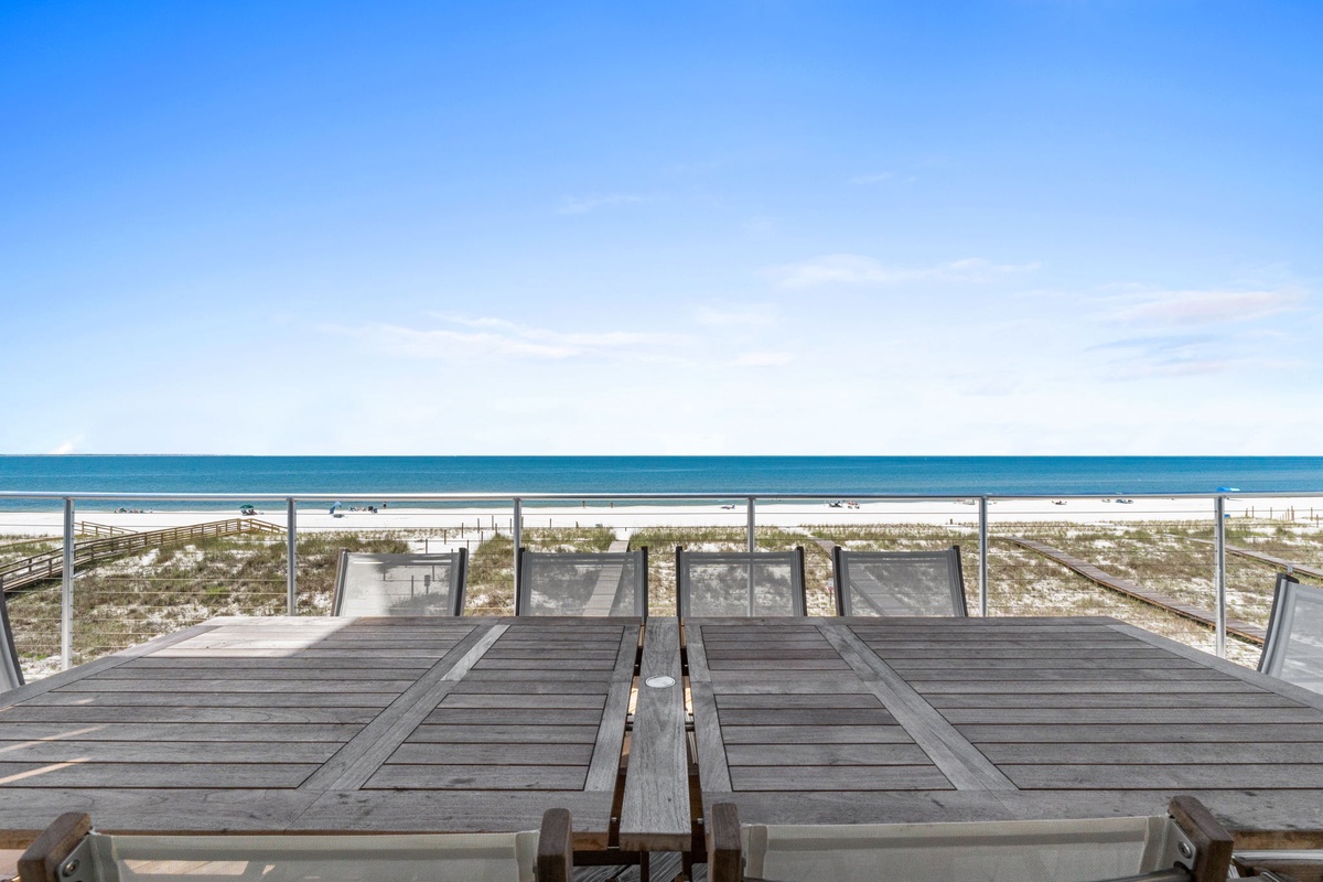 Beachfront deck with unobstructed views of white sand and turquoise water, offering direct access to the shore from the property.