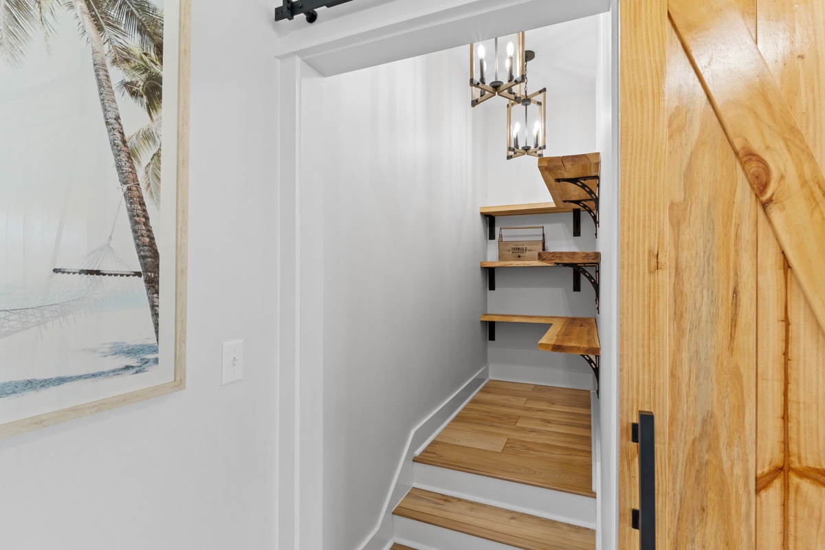A thoughtfully designed nook with wooden shelving creates functional storage space, accented by warm lighting and coastal artwork that invites you to settle in.