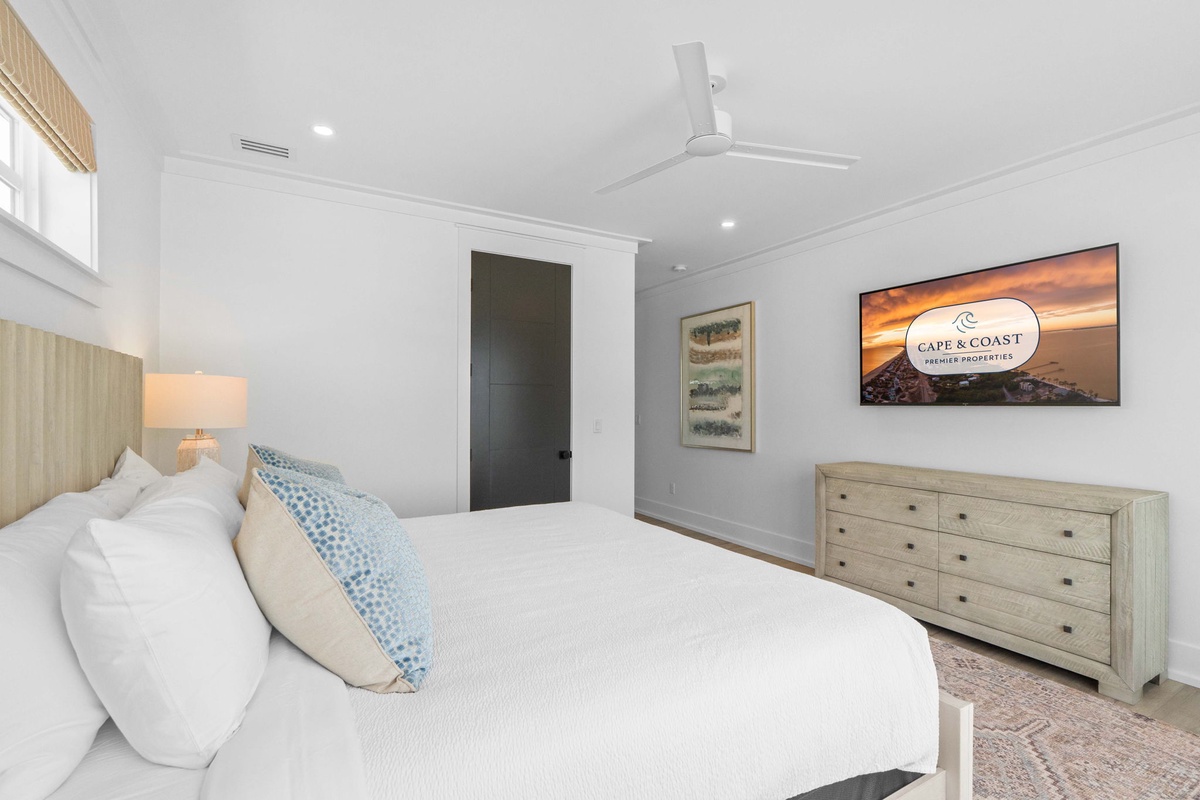Sink into your plush bed beneath the gentle breeze of the ceiling fan, where coastal artwork and soft lighting create your perfect retreat.