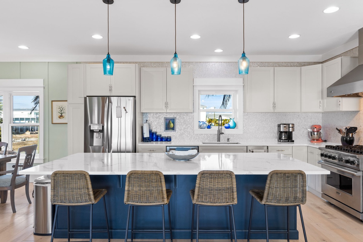 Your gourmet kitchen features a stunning blue island, stainless steel appliances, and coastal pendant lighting perfect for cooking memorable meals together.
