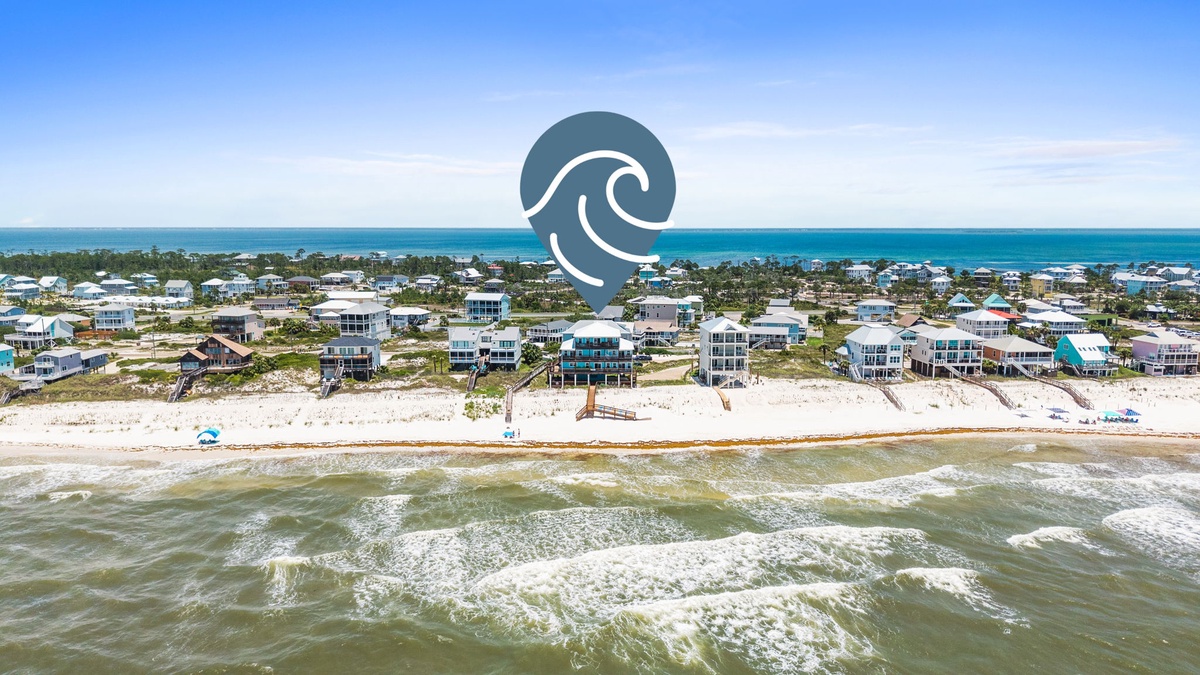 Aerial view of a beachfront community with modern vacation homes nestled between pristine sandy shores and calm turquoise waters, offering easy coastal access.
