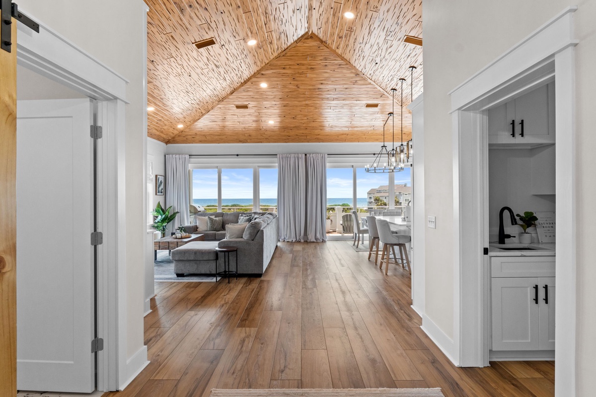 Step into soaring vaulted ceilings with warm wood planks that frame breathtaking ocean views, where your open-concept living and dining space invites endless seaside relaxation.
