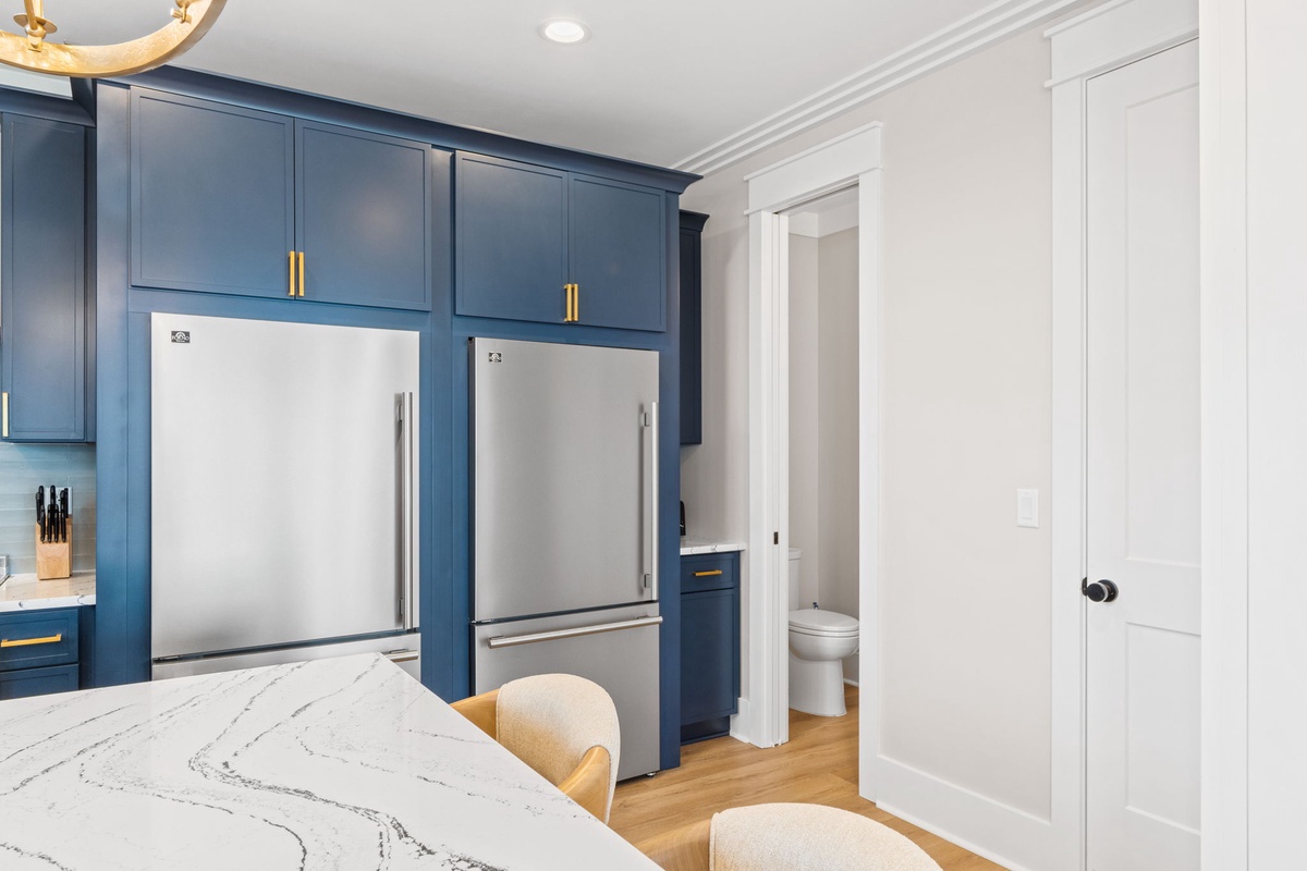 Your stylish kitchen features deep blue cabinetry with gold accents, twin stainless steel refrigerators, and a gorgeous marble island—perfect for preparing meals and gathering with loved ones.
