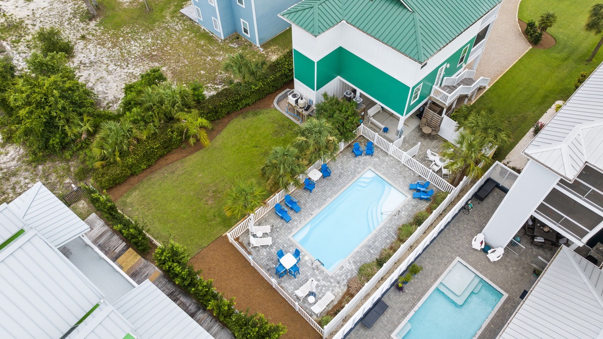 Aerial view of the vacation rental property featuring a private swimming pool, spacious lawn, and coastal architecture set among neighboring beach homes.