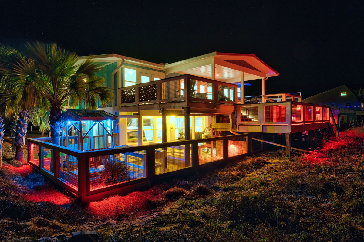 Modern beachfront property illuminated at night with colorful LED lighting and palm trees creating a tropical paradise atmosphere.