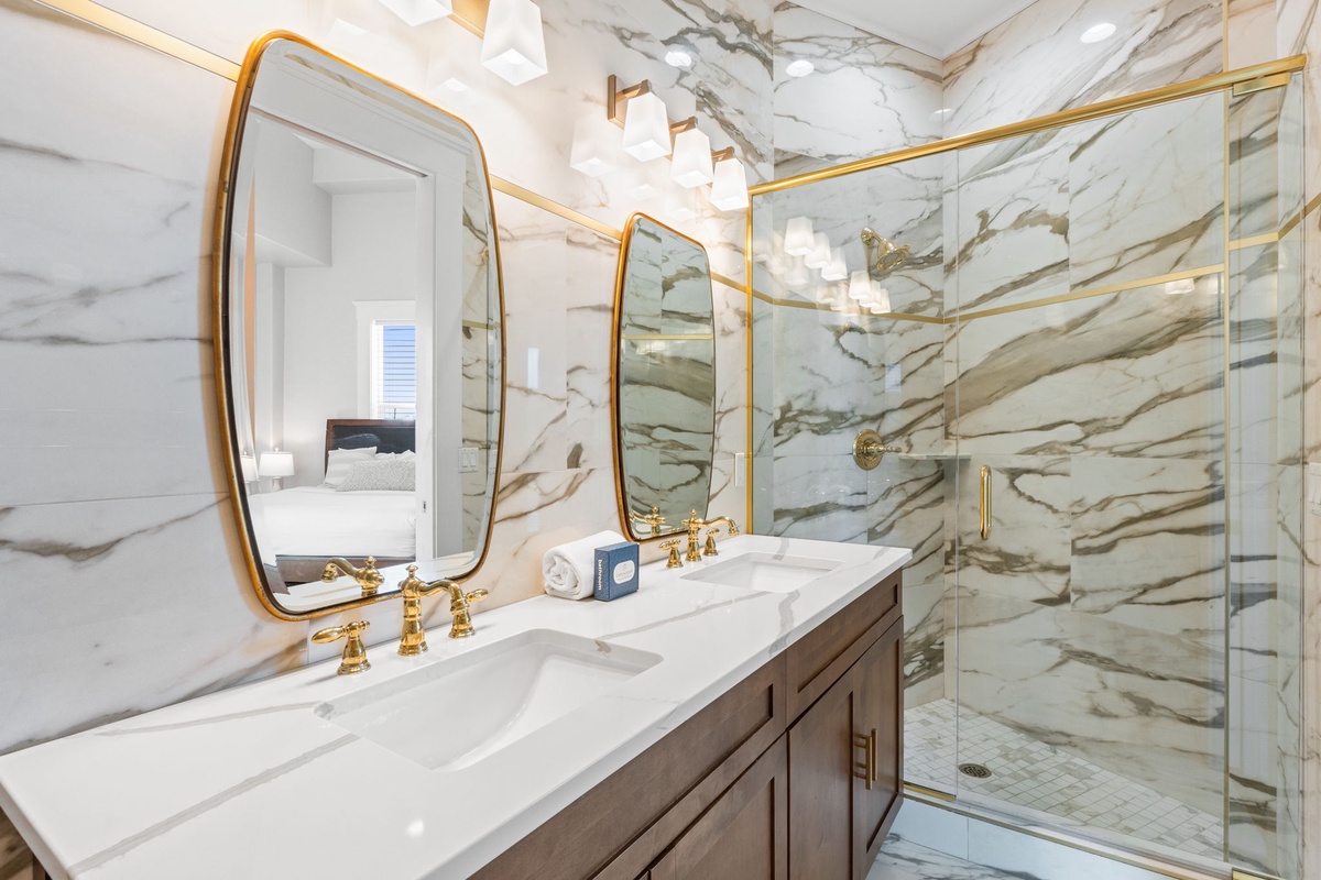 Indulge in luxury with this stunning marble bathroom featuring dual vanities, gold fixtures, and an elegant glass shower.
