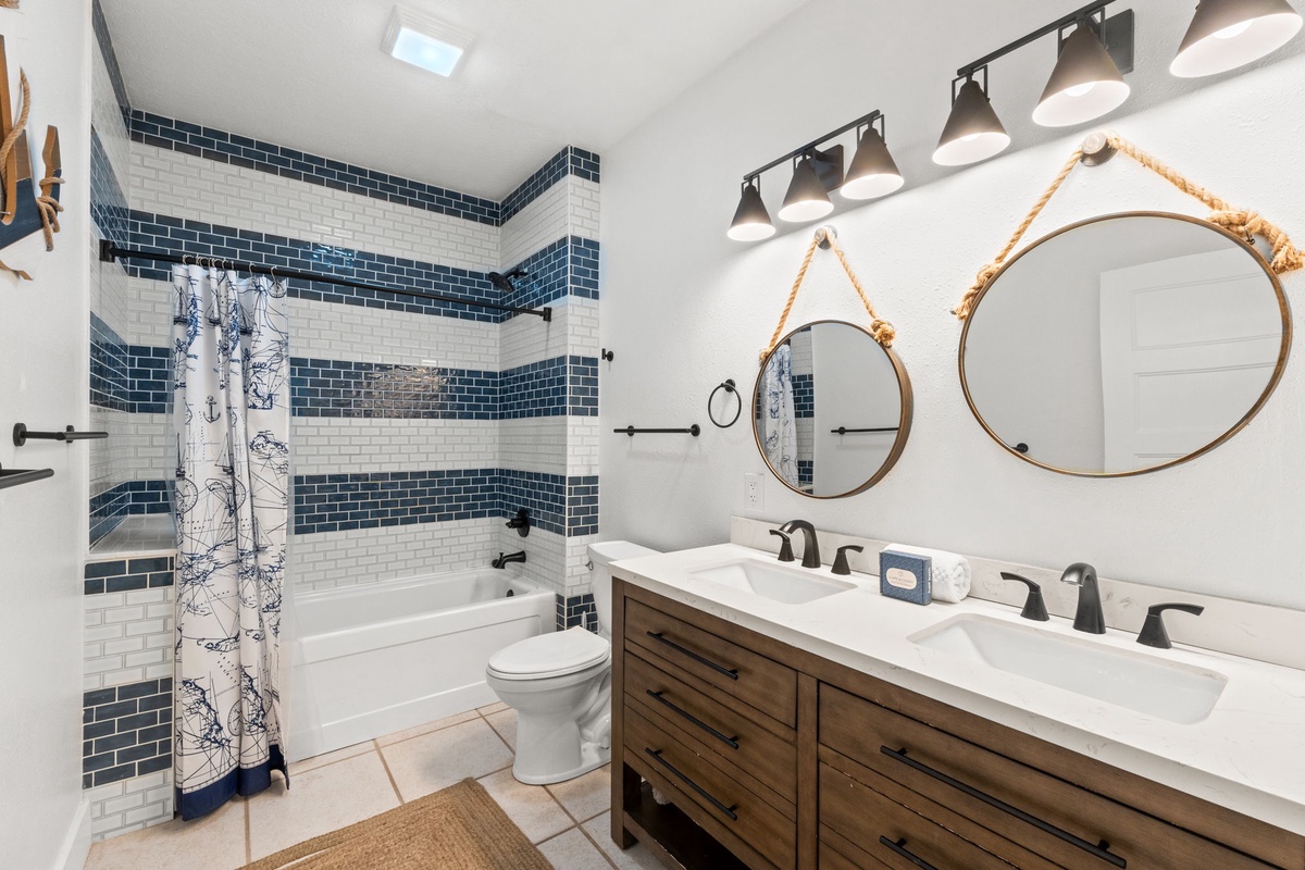 Step into this nautical-inspired bathroom featuring navy-and-white subway tile, dual vanities with rope-hung mirrors, and a spacious tub—perfect for unwinding after a day of coastal adventures.