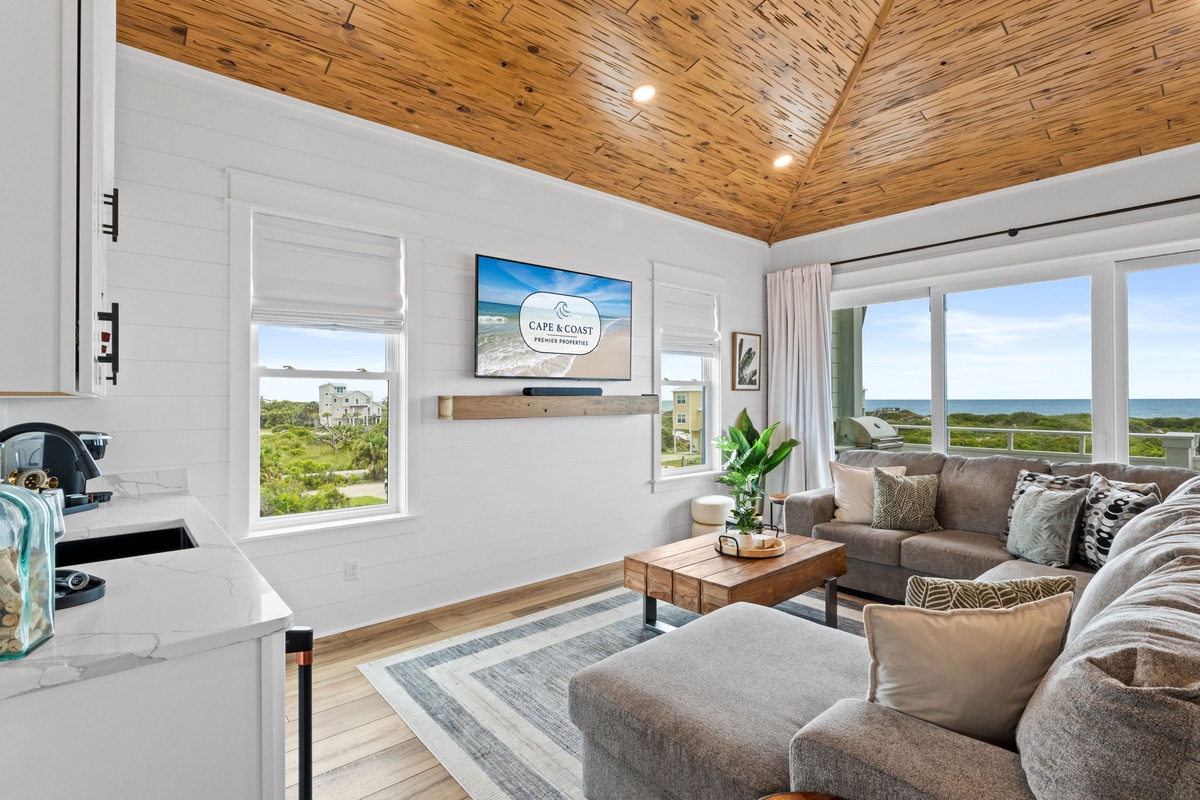 Relax in your sunlit living space with stunning ocean views, vaulted wood ceilings, and cozy seating perfect for unwinding after a beach day.