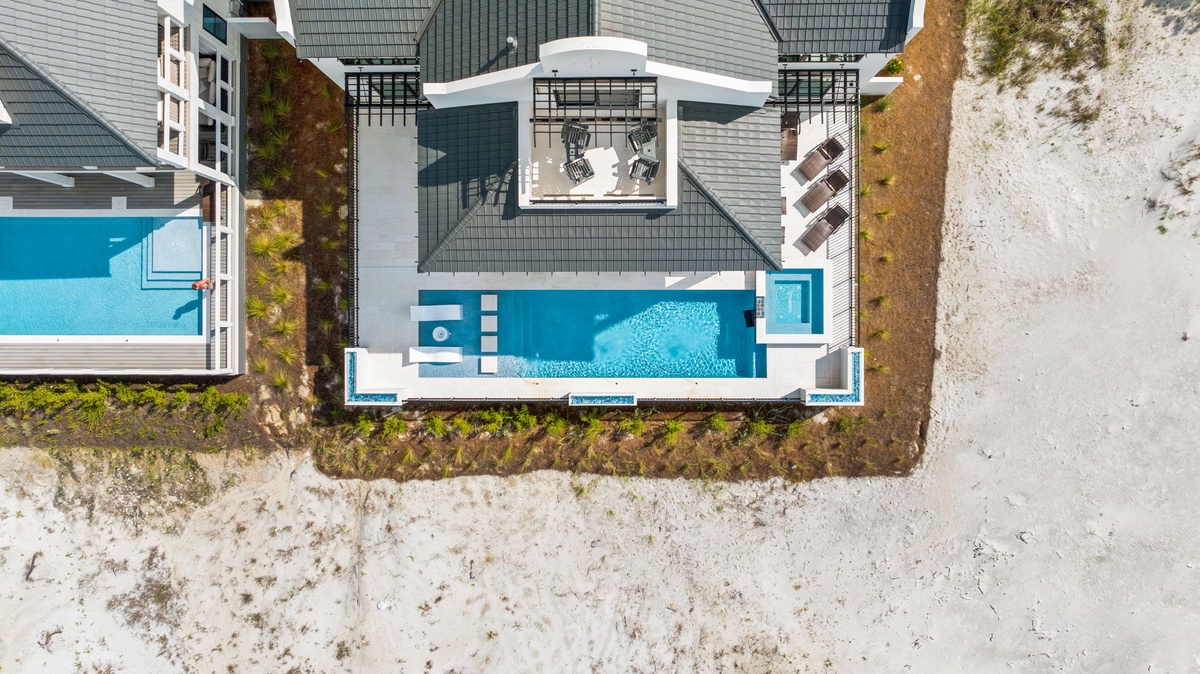 Aerial view of a modern beachfront vacation property featuring a private pool, outdoor dining terrace, and direct access to pristine white sand beaches.