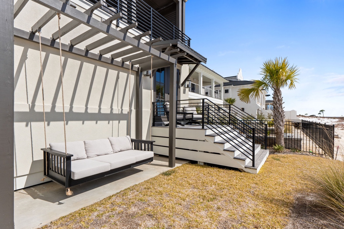 Relax on your private swing bed beneath the covered patio, surrounded by coastal landscaping and modern comfort.