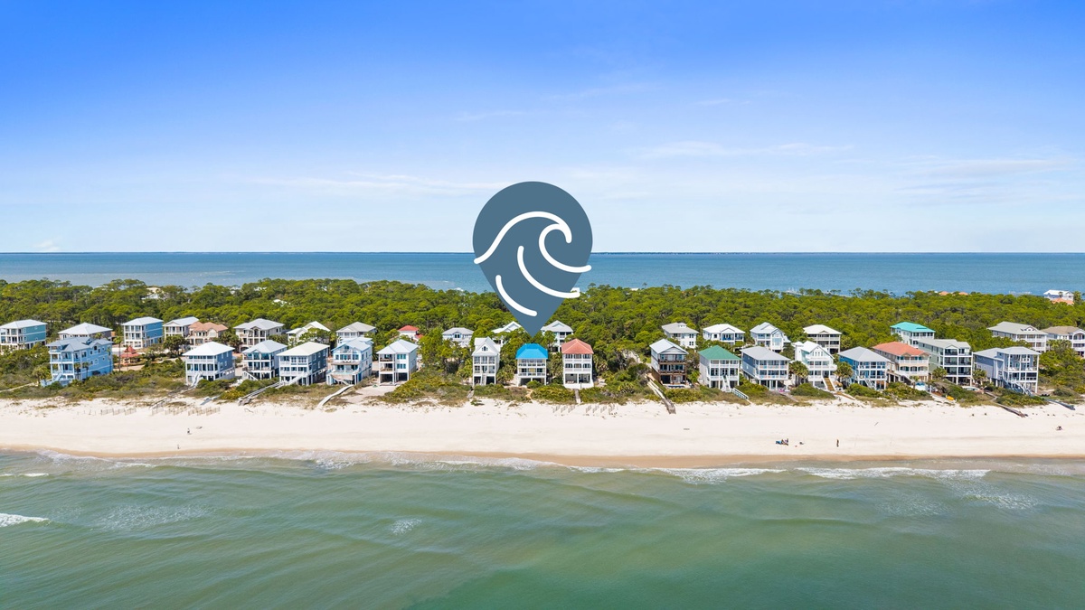 Aerial view showcasing beachfront rental homes nestled between pristine coastline and lush greenery along this stunning stretch of beach.