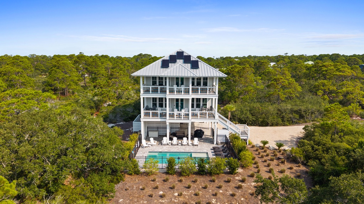 An elevated coastal home featuring modern architecture with solar panels nestled privately among lush maritime forest, complete with a sparkling pool and spacious outdoor gathering areas.