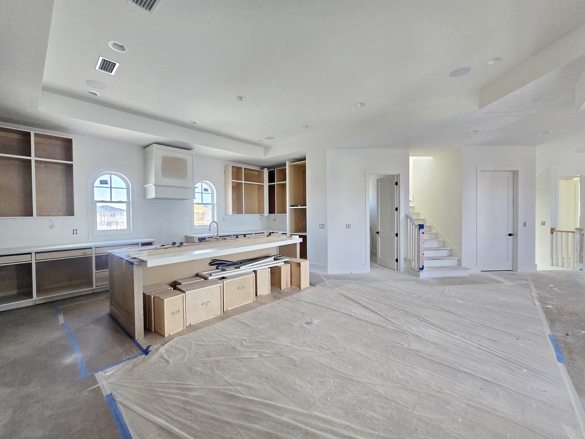 Modern kitchen under construction with spacious island, custom cabinetry, and open-concept design connecting to living areas.