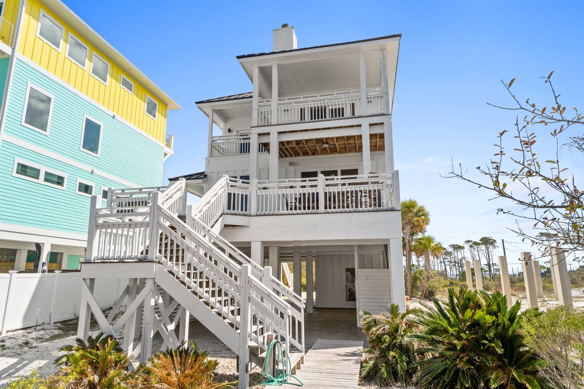 Multi-story beachside property with elevated design, surrounded by colorful coastal homes and tropical landscaping.