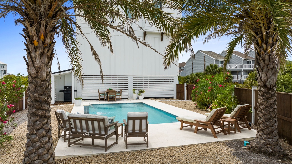 A private outdoor escape framed by swaying palms with a sparkling pool, lounge chairs, and shaded seating areas for relaxing in sun or shade.