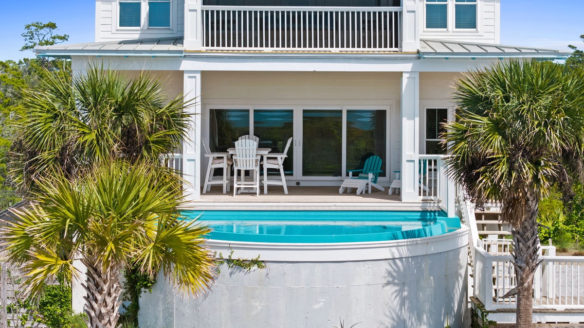 Modern coastal property featuring a pristine swimming pool surrounded by tropical palm trees, with multiple levels and covered outdoor seating areas.