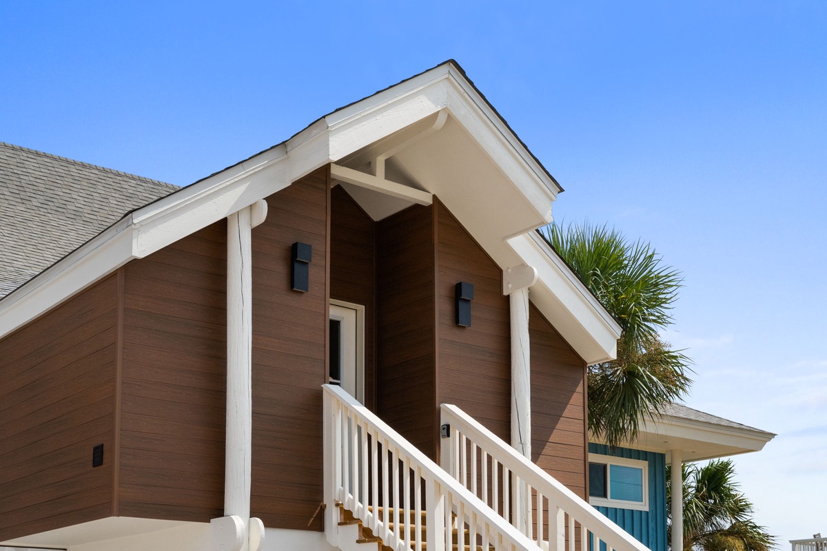 A welcoming coastal exterior featuring warm wood tones, crisp white trim, and tropical palms in a tranquil beachside setting.
