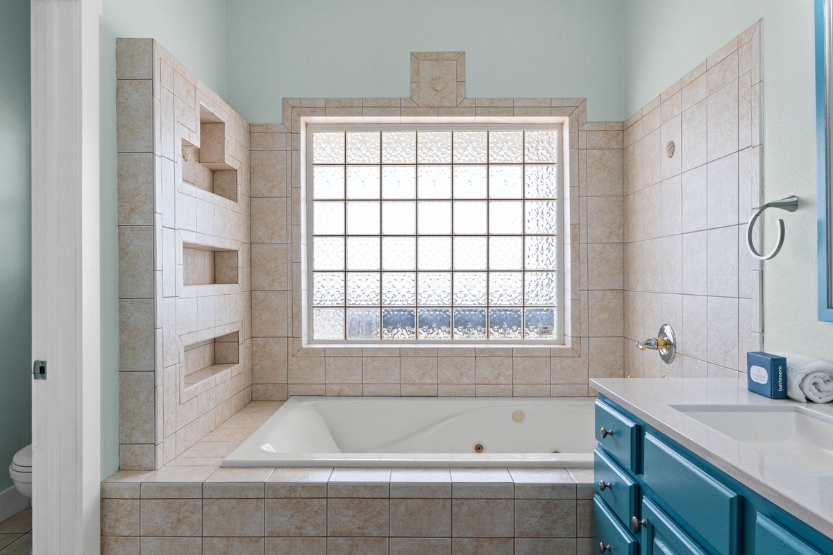Unwind in your private spa-like bathroom, where a deep soaking tub beneath a frosted window invites relaxation. Built-in shelves keep everything you need within reach for a truly serene escape.