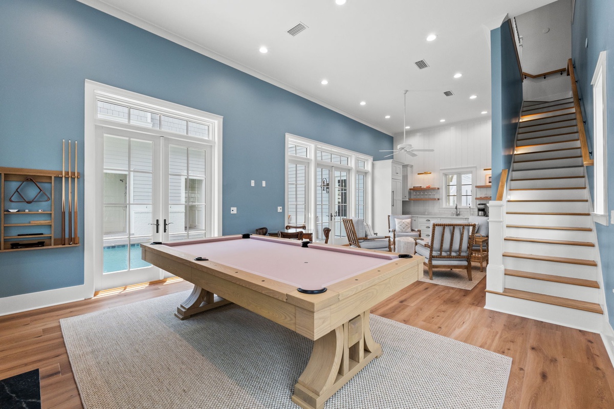 Your game room and billiard table await, where laughter and friendly competition blend with coastal charm, all bathed in natural light and overlooking the pool.