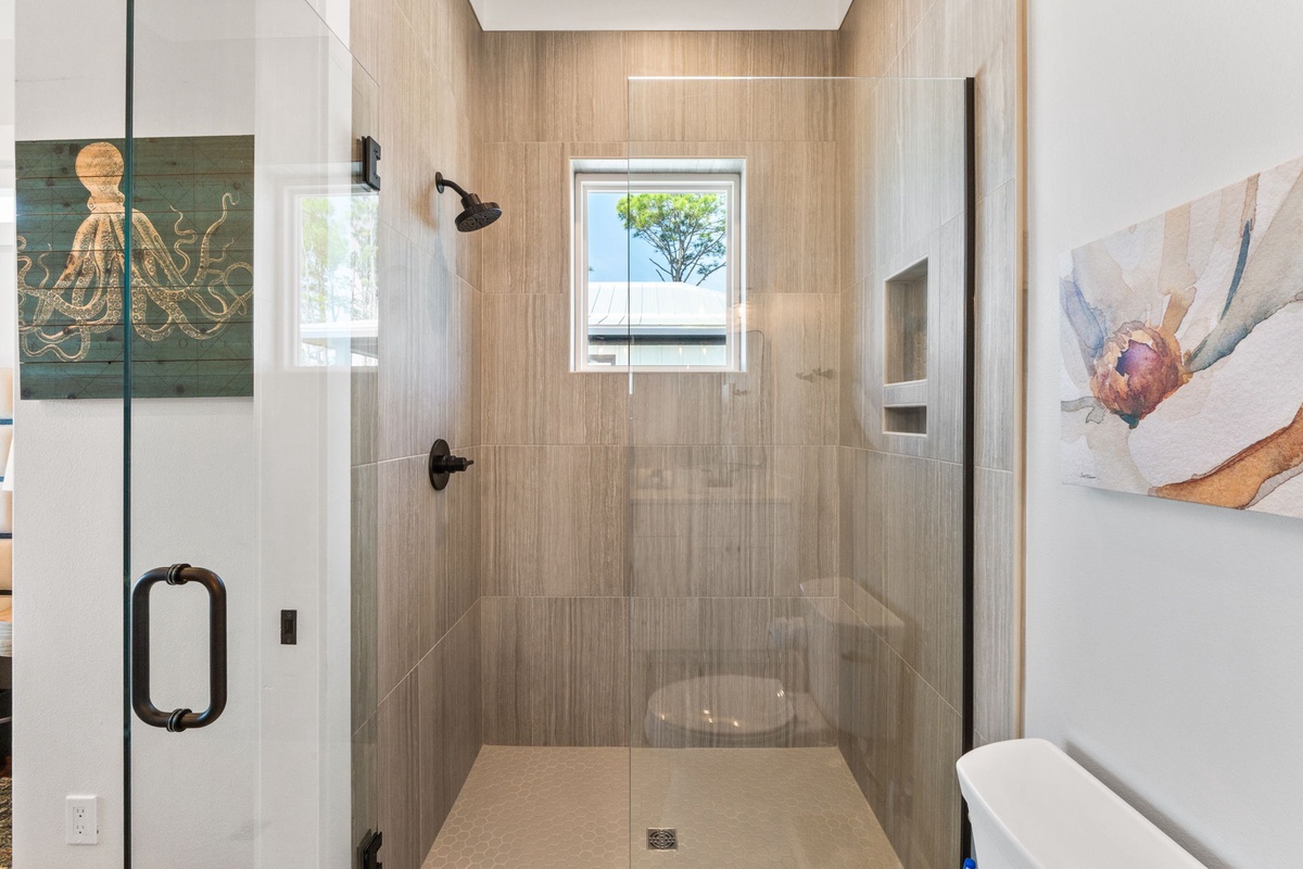 Step into your spa-like glass shower with warm wood-grain tiles and natural light streaming through the window.