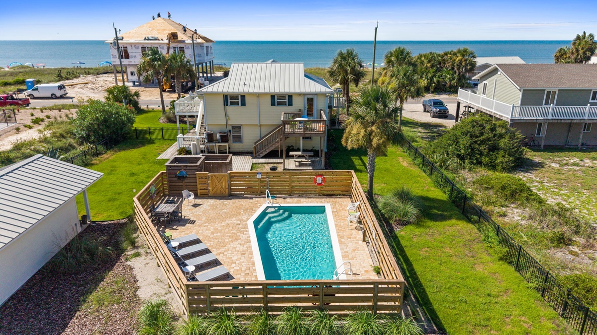 Aerial view of a beachside vacation home featuring a private swimming pool, outdoor lounging spaces, and direct access to pristine coastal surroundings just steps from the shore.