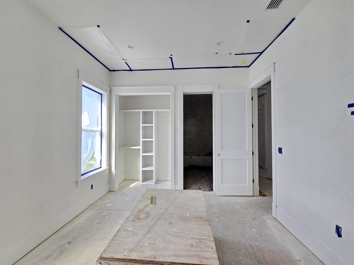 An unfurnished room in the final stages of finishing, featuring fresh white walls, a built-in closet with shelving, and large windows that invite natural light into your future retreat.