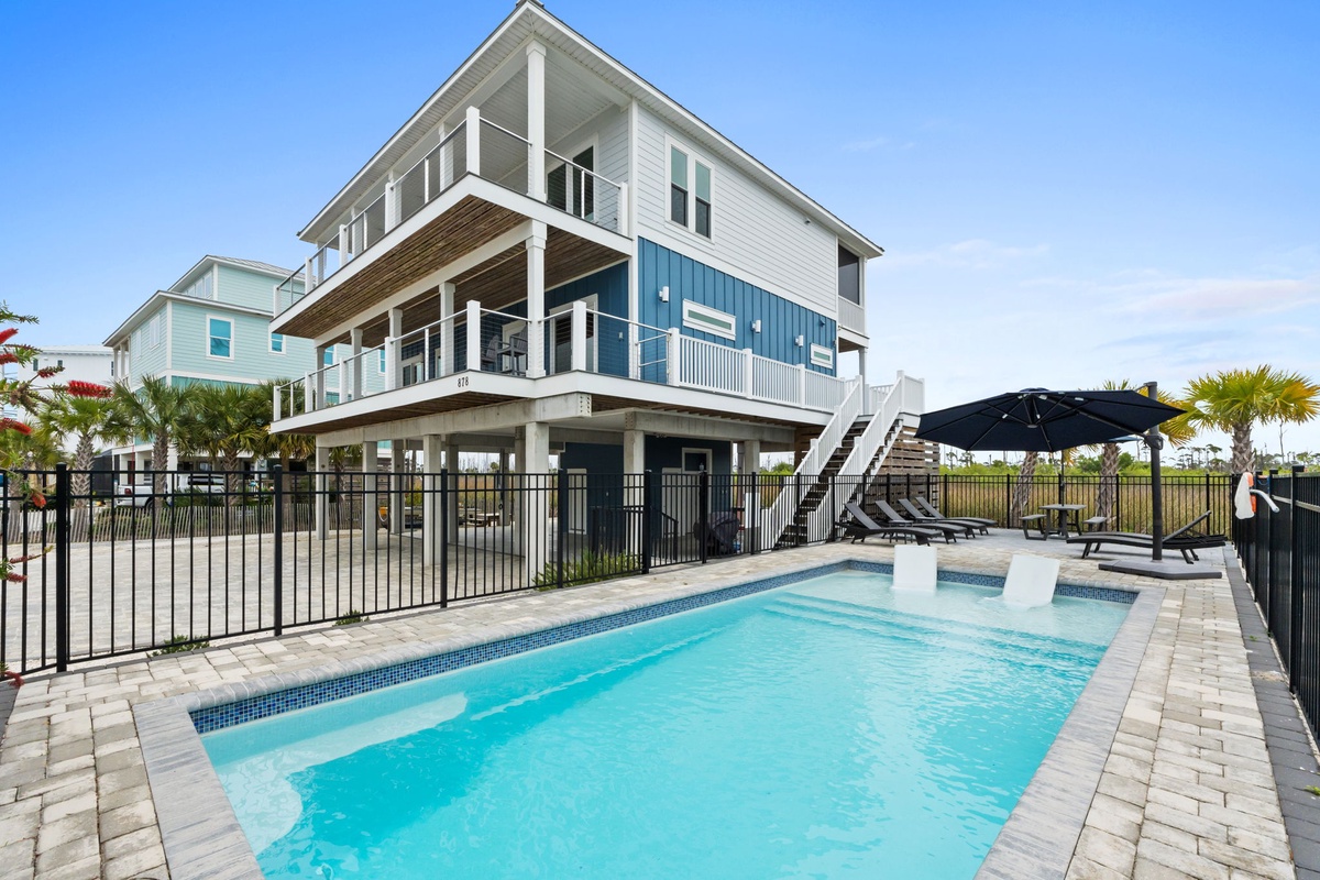Modern coastal home featuring a sparkling private pool, elevated design, and bright blue accents under clear Florida skies.