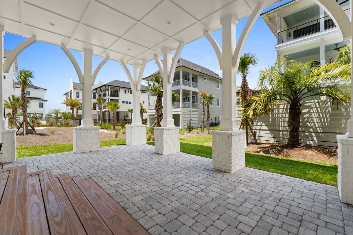 A covered patio with elegant white columns overlooks landscaped grounds and surrounding vacation homes, offering a shaded outdoor retreat for relaxing and entertaining.