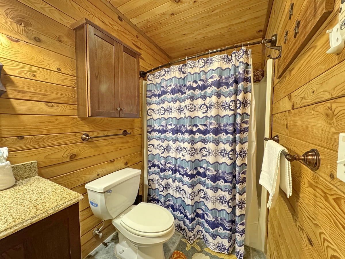 Cozy log cabin bathroom with rustic wood walls and nautical-themed shower curtain creates your perfect mountain retreat atmosphere.
