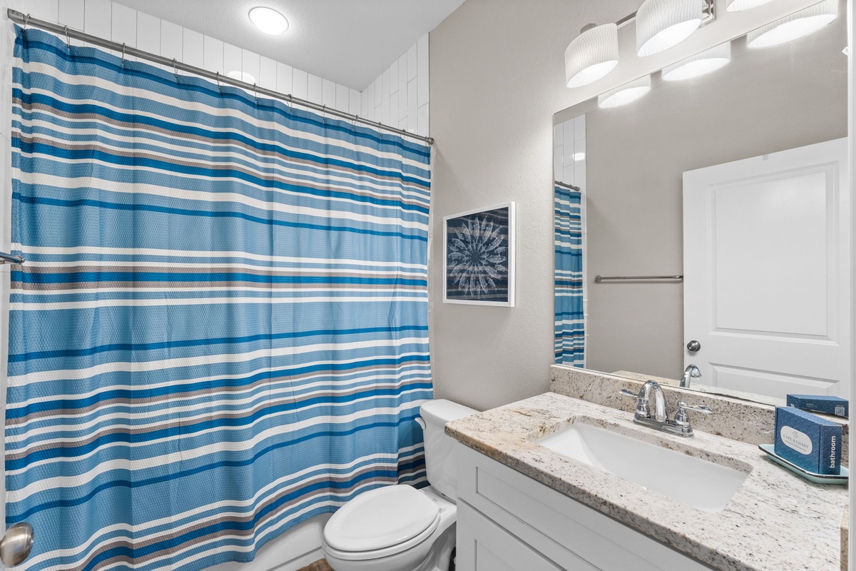Refresh in your private bathroom with coastal blue striped shower curtain, granite countertops, and modern vanity lighting for your comfort.