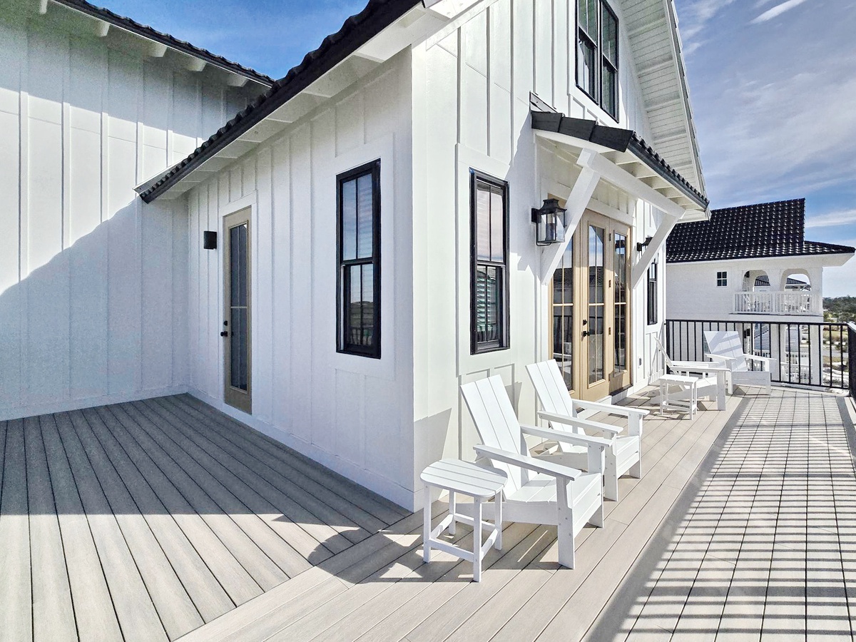 Modern farmhouse-style vacation rental featuring white board-and-batten siding, black-framed windows, and a wraparound deck.