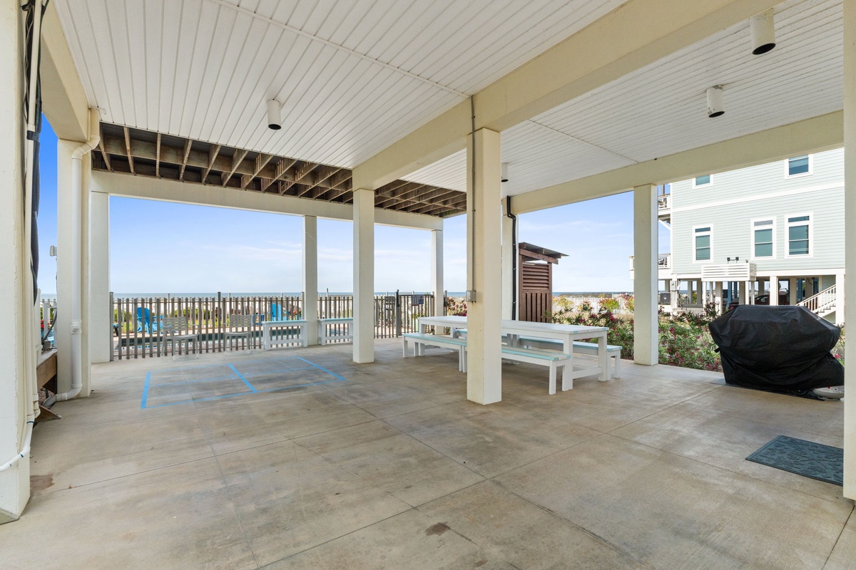 A ground-level covered outdoor area beneath the property, offering coastal views, bench seating, and access to nearby beachfront amenities.