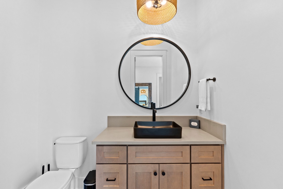 Your modern bathroom features a sleek vessel sink beneath a striking round mirror, perfectly lit by a warm woven pendant. Fresh towels and clean lines create a spa-like retreat.