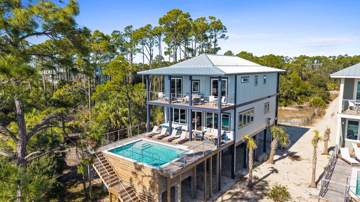 Modern coastal home with elevated pool deck surrounded by lush pine forest offering peaceful retreat setting.