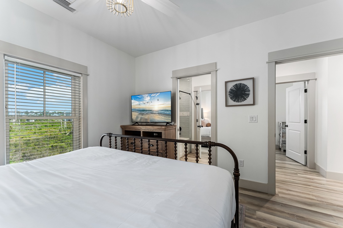 Your peaceful bedroom features a comfortable bed, wall-mounted TV for evening entertainment, and bright windows with beautiful natural views.