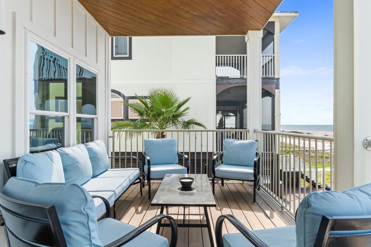 Your private balcony offers coastal breezes and ocean glimpses, framed by soft blue cushions and natural wood—a tranquil retreat where morning coffee feels like pure escape.