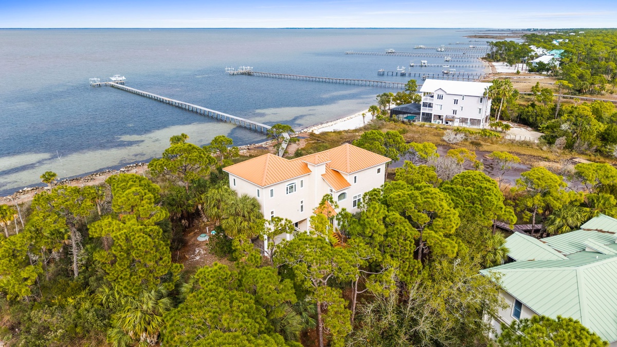 Stunning waterfront property nestled among lush trees, with private pier access and serene bay views stretching to the horizon.