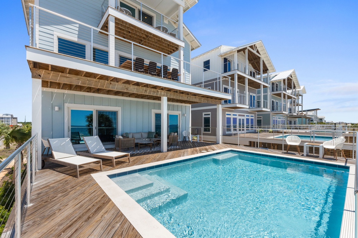 The exterior of this modern vacation property showcases multiple units with a shared swimming pool, surrounded by coastal-style architecture and ocean breezes.